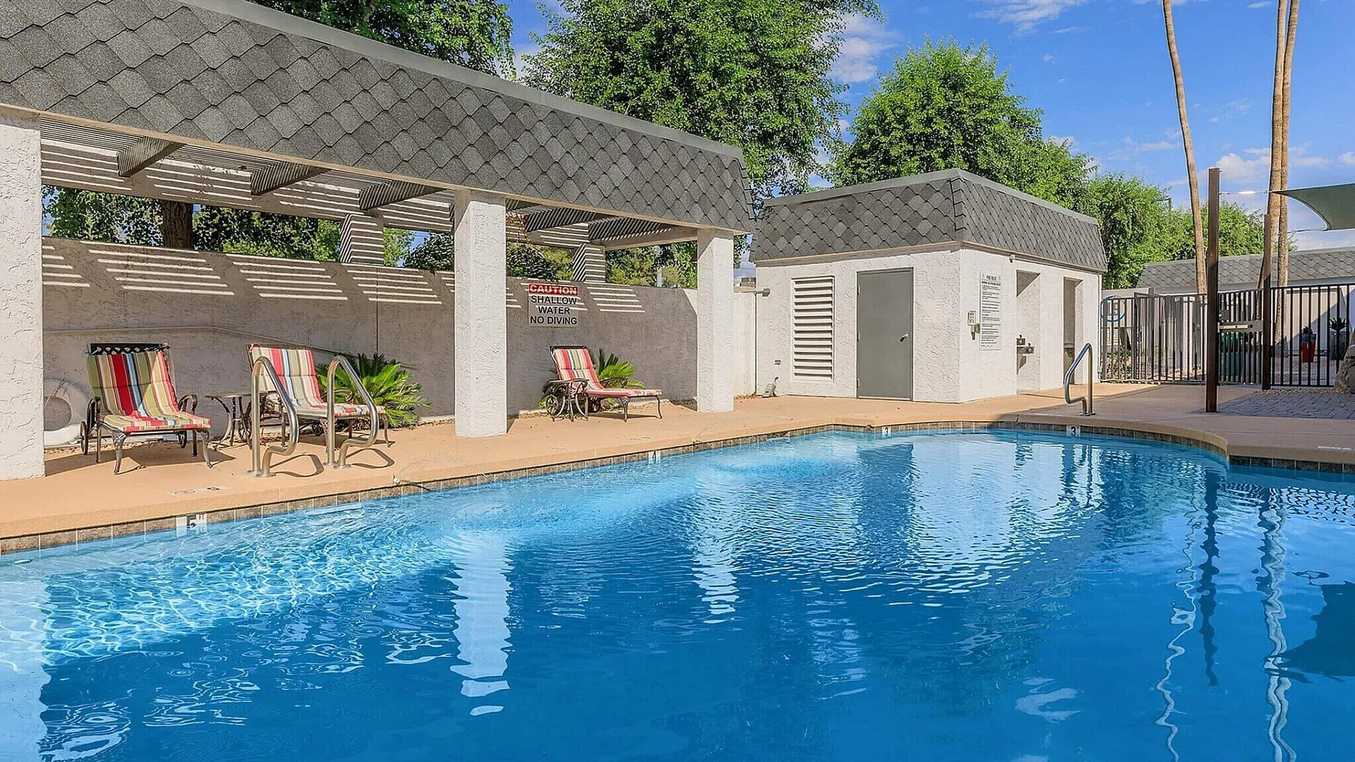 Inviting outdoor pool area with comfortable lounge chairs and shaded seating, perfect for relaxation and leisure under a clear blue sky.