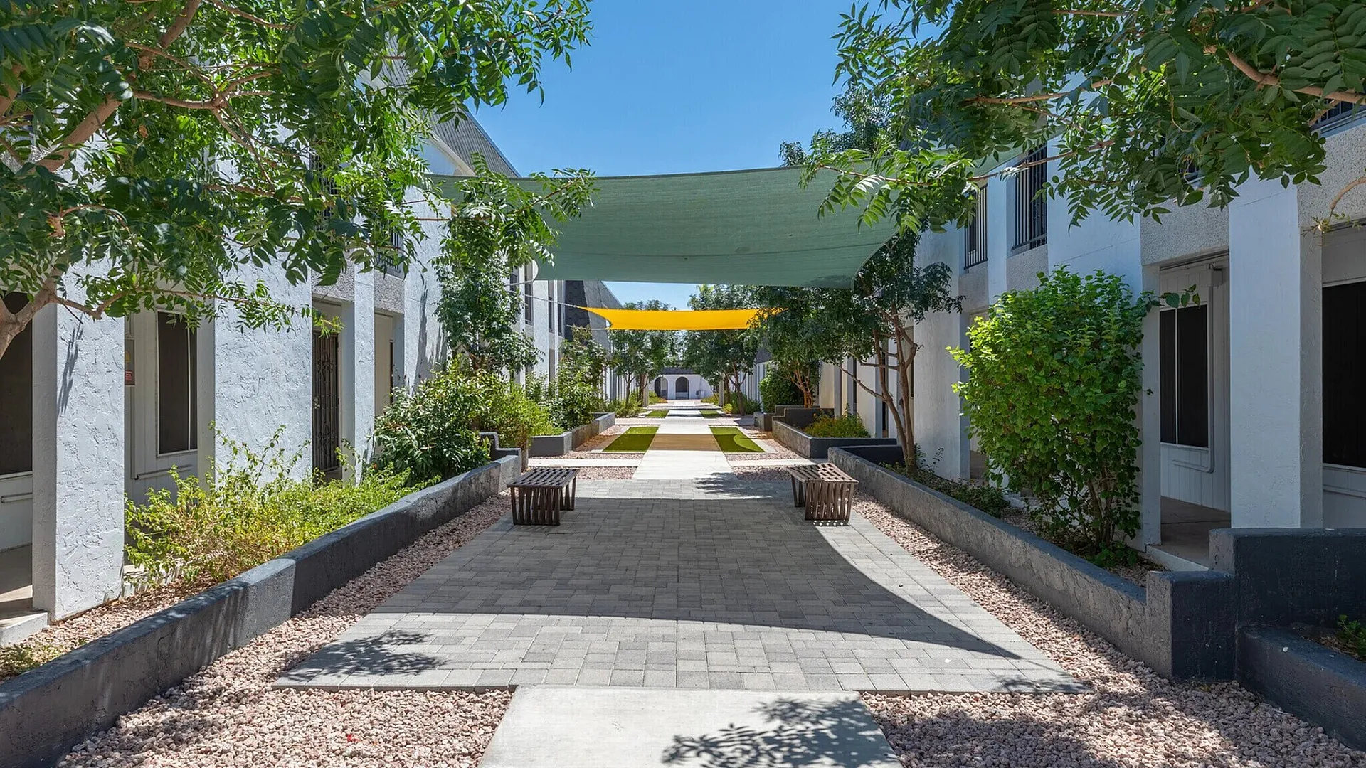 Beautifully landscaped courtyard with greenery and shaded walkways, offering a serene and inviting atmosphere in a modern apartment complex.