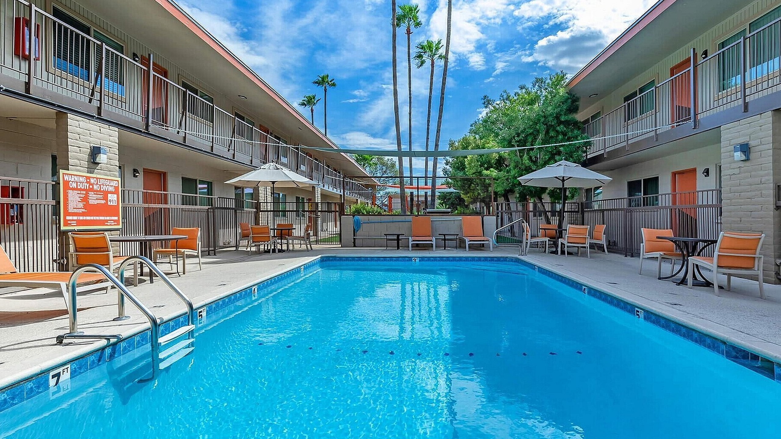 Inviting apartment complex with a sparkling pool, surrounded by lounge chairs and patio seating under bright blue skies.
