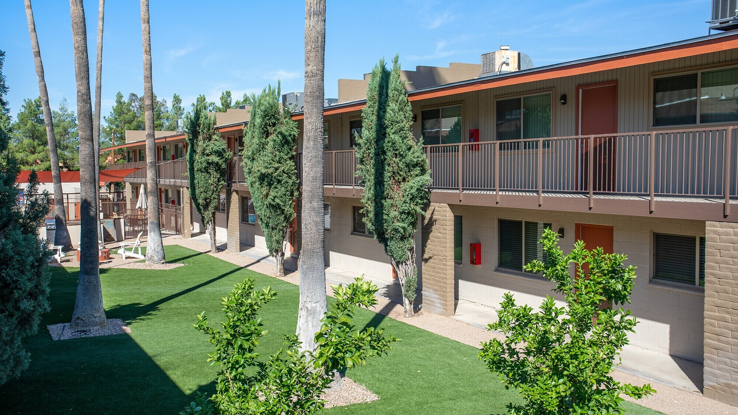 Charming apartment complex with lush landscaping, modern architecture, and inviting outdoor spaces under clear blue skies.