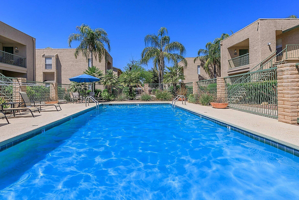 Inviting outdoor scene featuring a sparkling pool surrounded by modern apartment buildings and lush palm trees under a clear blue sky.