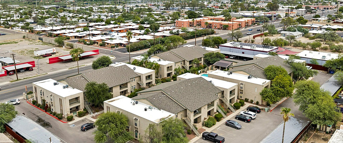 Scenic aerial view of a modern apartment complex with mountain backdrop, featuring lush greenery and ample parking.