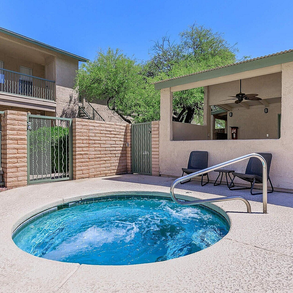 Inviting apartment courtyard featuring a refreshing hot tub, cozy outdoor seating, and modern architectural design under clear blue skies.