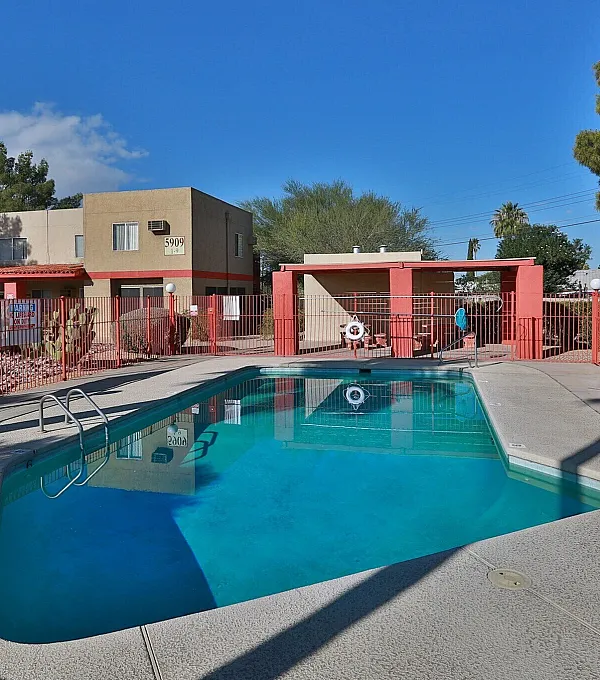 Inviting outdoor pool area with vibrant red fencing, adjacent to a modern apartment building under a clear blue sky.