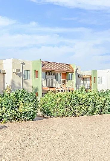 Charming apartment complex with colorful facades, lush greenery, and a serene atmosphere under a clear blue sky.