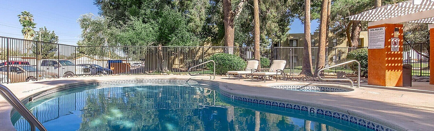 Tranquil apartment community pool surrounded by lush greenery and inviting lounge chairs.