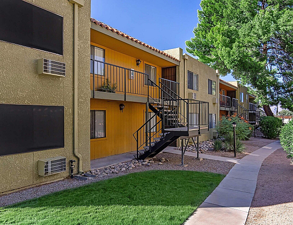 Charming apartment complex with vibrant yellow accents, surrounded by lush greenery and modern exterior staircases.