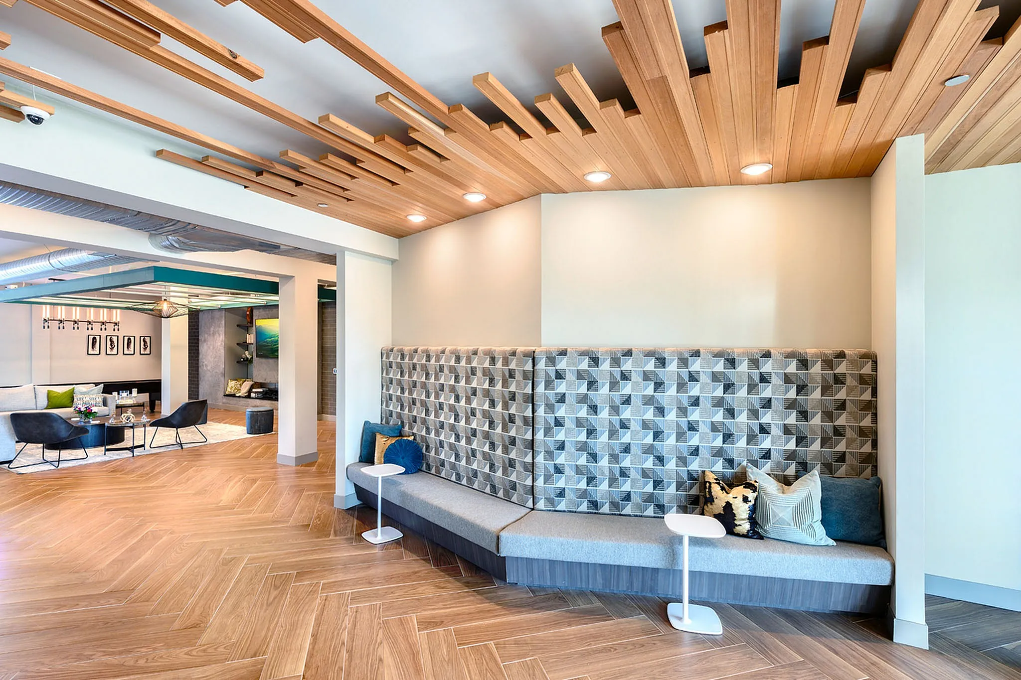 Modern lounge area showcasing a chic geometric bench with plush cushions, elegant wooden ceiling accents, and stylish herringbone flooring.