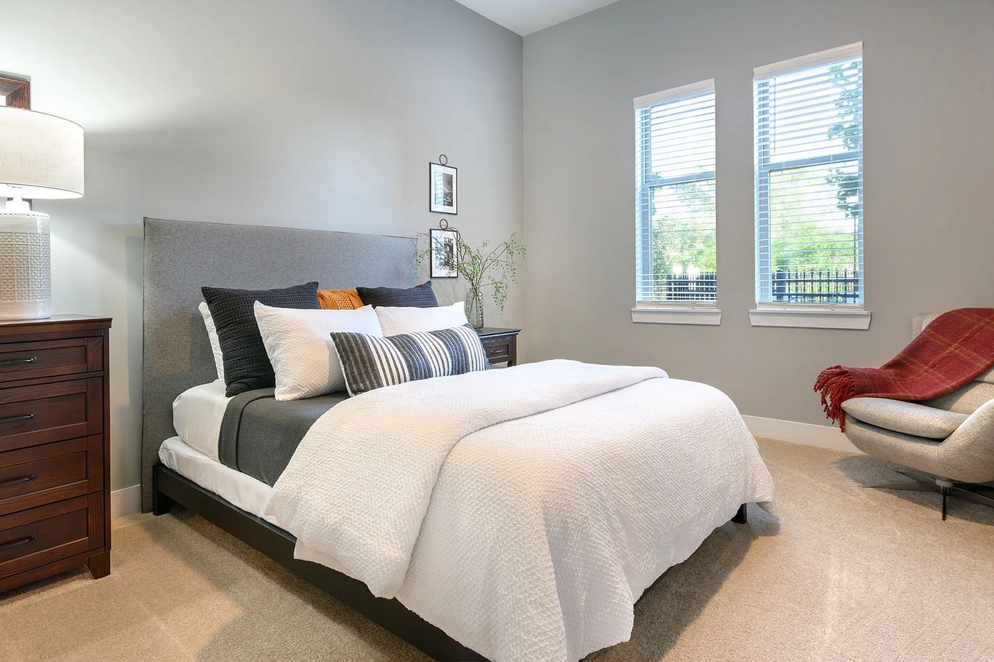 Inviting bedroom with stylish decor, featuring a plush bed, modern gray headboard, and natural light streaming through large windows.