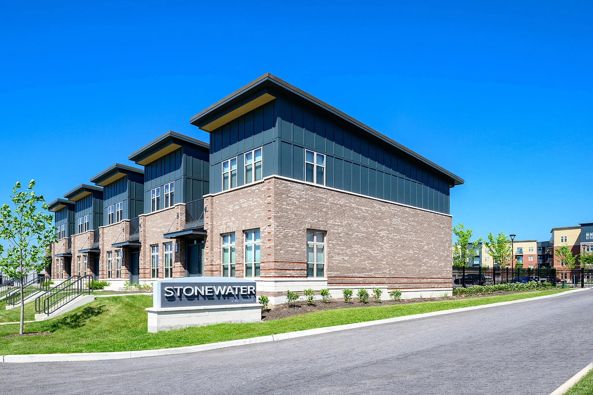 Modern brick townhouse complex with sleek architectural design and well-maintained landscaping under a clear blue sky at Stonewater.