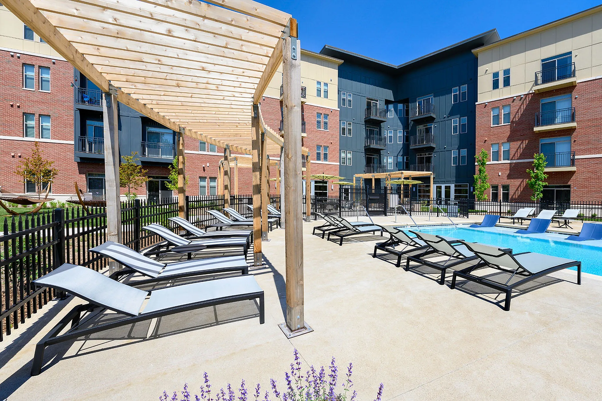 Modern apartment complex featuring a luxurious outdoor pool area with sun loungers under stylish pergolas, surrounded by contemporary architecture.