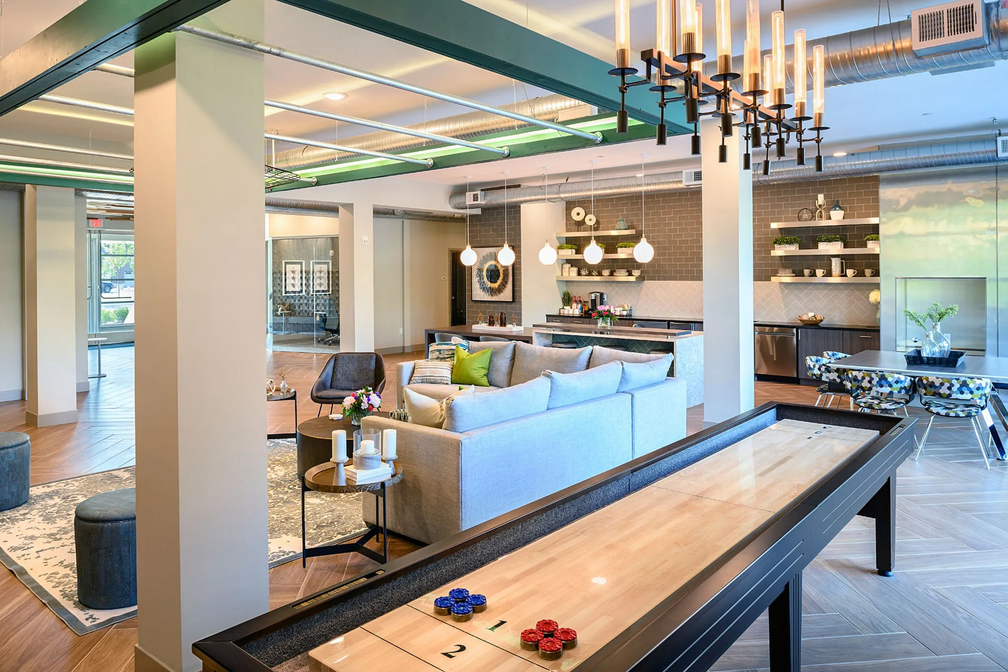 Modern communal apartment lounge with stylish seating, sleek kitchen, and a fun shuffleboard table under contemporary lighting.