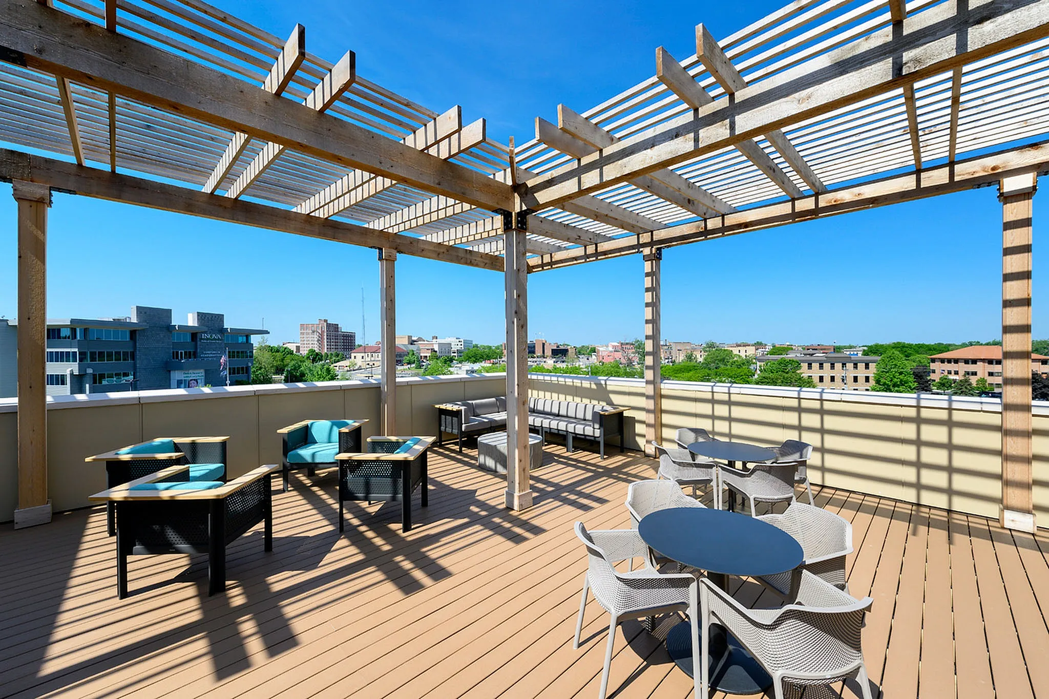 Elegant rooftop patio featuring stylish furniture, wood pergola, and expansive city views under a clear blue sky.