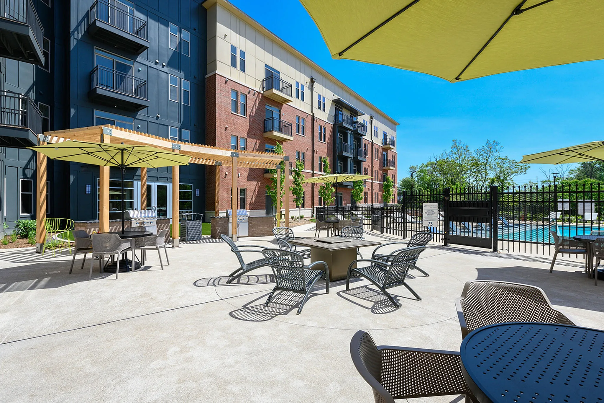 Modern apartment complex with spacious outdoor patio, stylish seating, and vibrant pool area under sunny sky.
