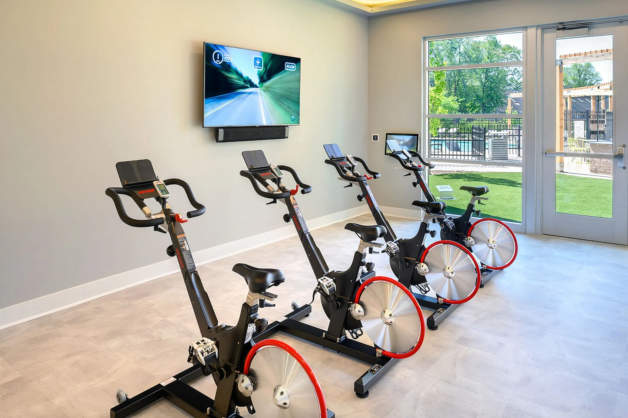 Bright and modern fitness room featuring high-tech stationary bikes and a large TV screen for enhanced workout experiences.