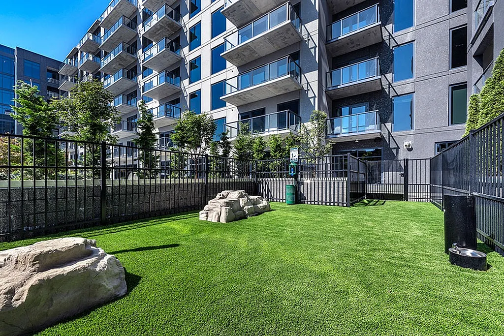 Modern apartment exterior with balconies and beautifully landscaped garden featuring vibrant green lawn and natural stone accents.
