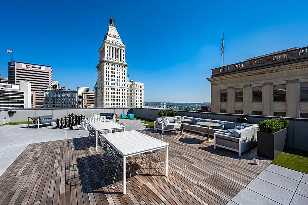 Luxurious rooftop patio featuring stylish lounge seating, modern tables, and a giant chess set against a stunning city skyline backdrop.