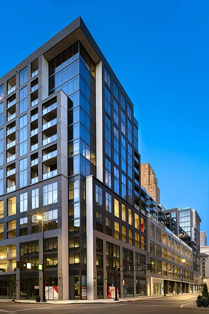 Modern high-rise building with sleek glass facade and illuminated windows against a vibrant evening sky.