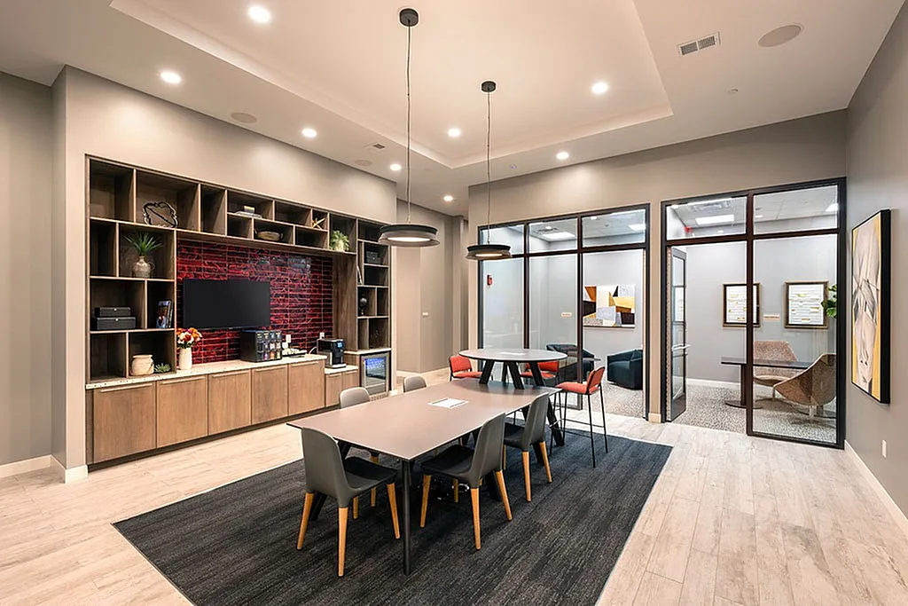 Contemporary office space featuring a sleek meeting table, modern decor, and a stylish lounge area with glass partitions.
