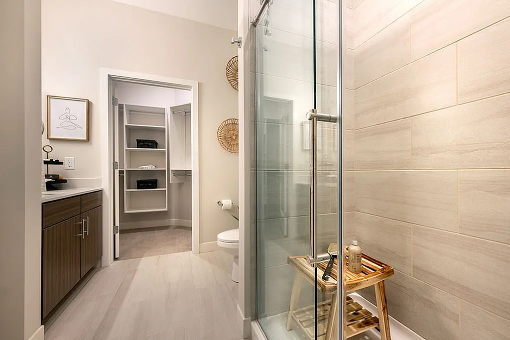 Modern bathroom with elegant shower, sleek vanity, and spacious walk-in closet, offering a luxurious living experience.