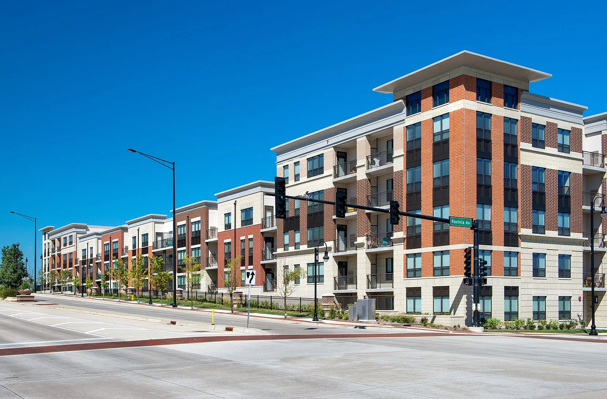 Modern apartment complex showcasing sleek architecture with balconies and lush greenery, bathed in bright sunlight.