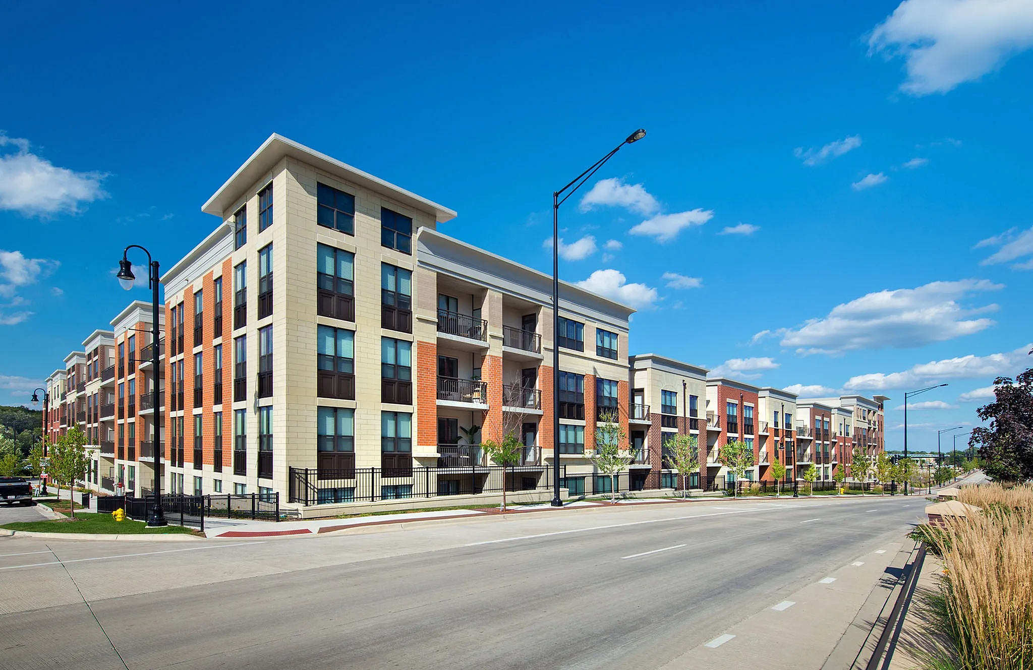 Modern apartment building with stylish architecture, featuring spacious balconies and vibrant surroundings under a clear blue sky.