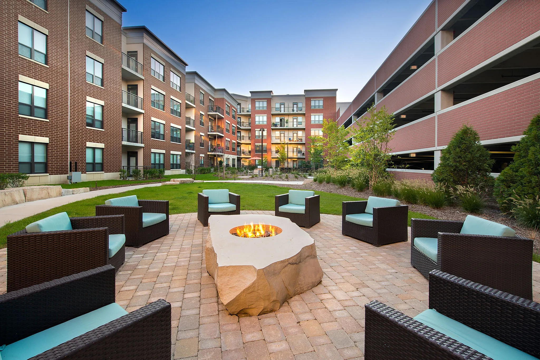 Chic outdoor courtyard with modern seating and a central fire pit, surrounded by contemporary brick apartment buildings, offering a serene and inviting environment for relaxation.
