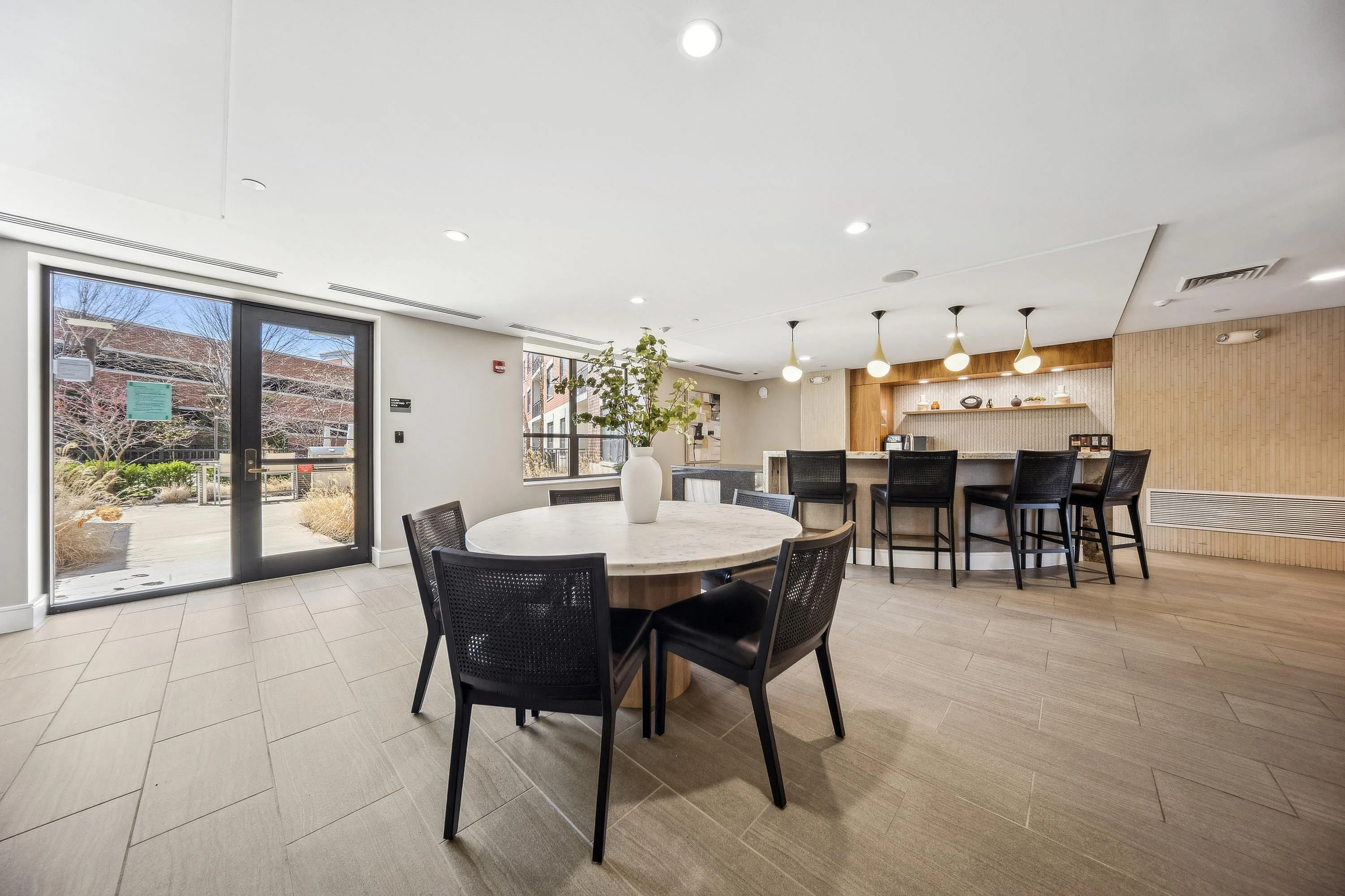Modern communal dining area with elegant round table, stylish chairs, and a chic bar setup with contemporary lighting.
