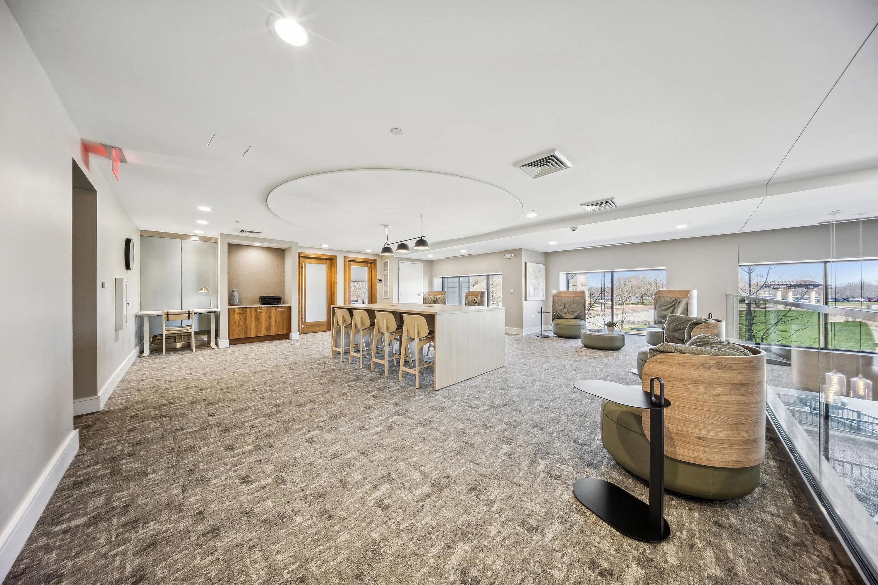 Elegant lounge space with modern decor, featuring a long communal table, plush seating, and panoramic windows overlooking lush greenery.