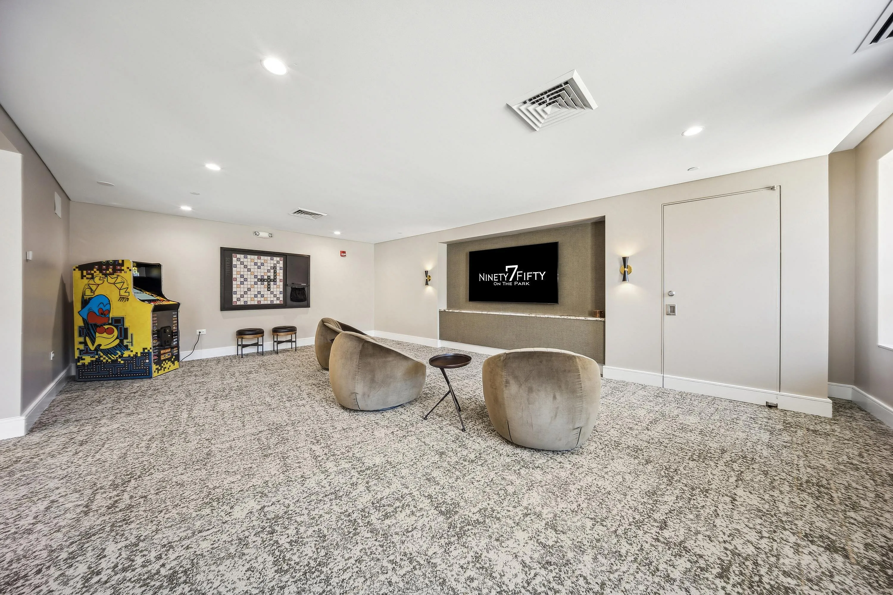 Chic entertainment lounge with cozy seating, vintage arcade game, and sleek screen at Ninety7Fifty on the Park.