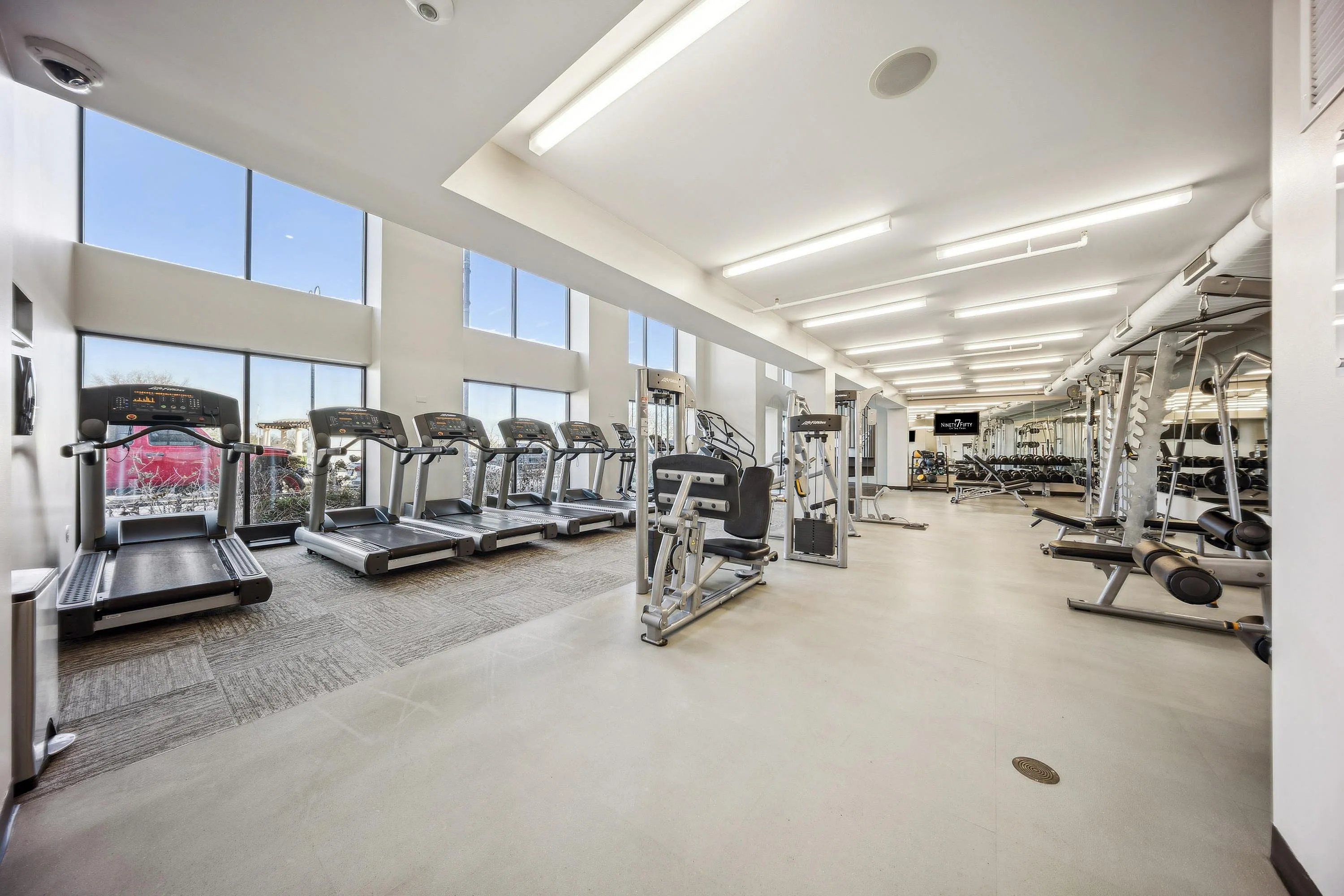 Bright and spacious gym with state-of-the-art equipment, large windows, and ample natural light in a modern apartment building.