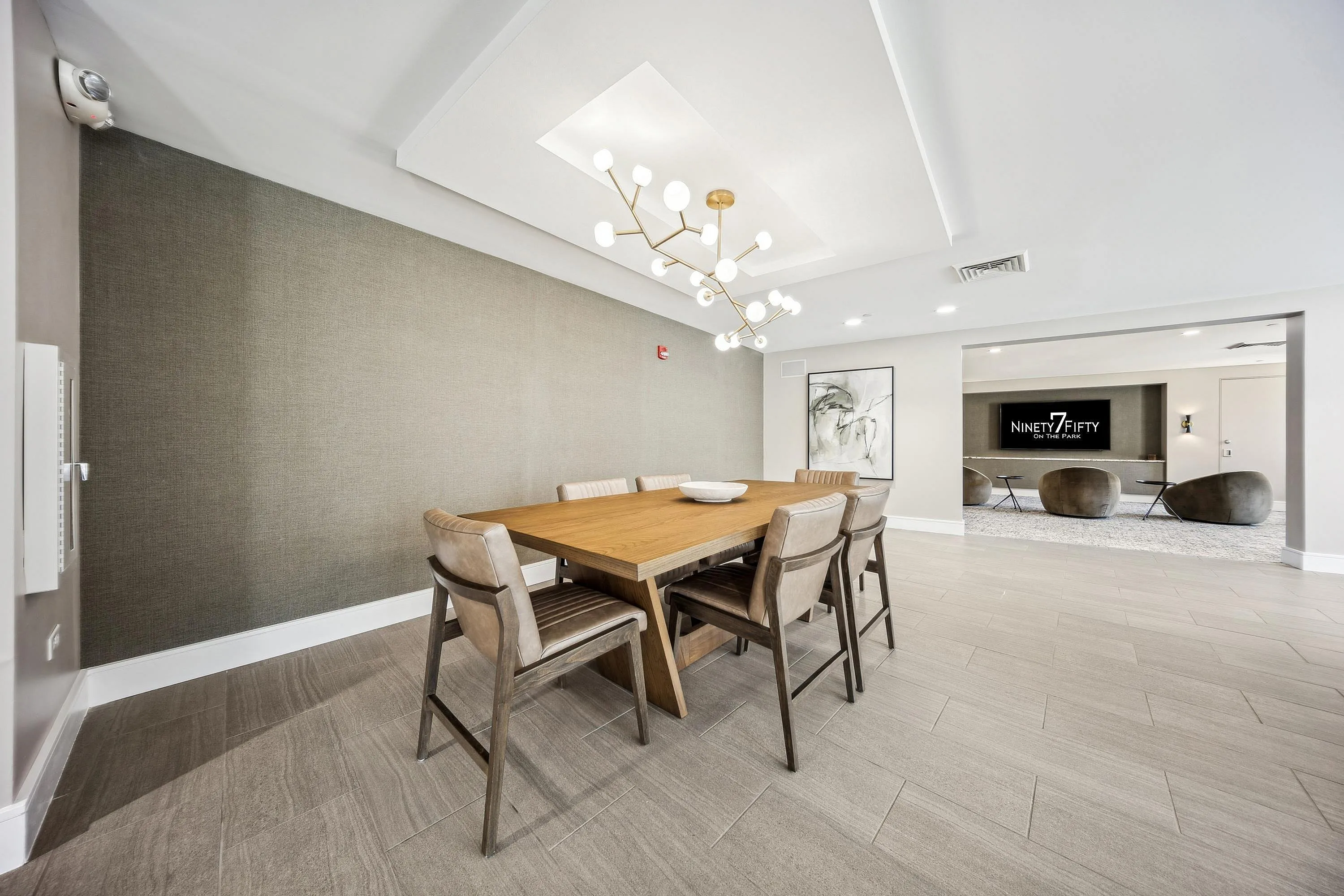 Modern dining room with elegant wooden table and sleek chairs, featuring a contemporary chandelier and stylish neutral decor.