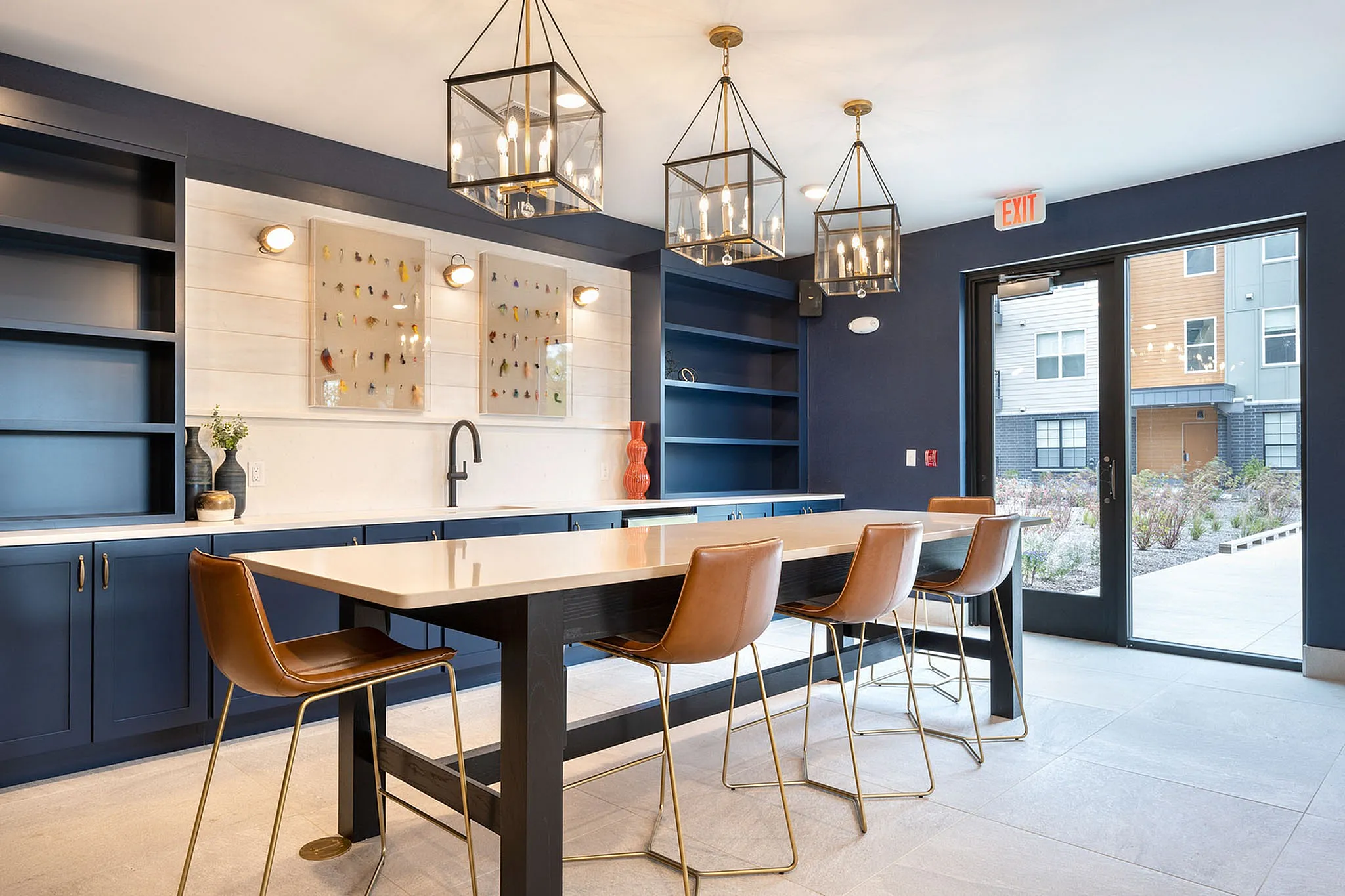 Elegant modern kitchen area with stylish navy cabinets, chic pendant lighting, and a spacious island with leather stools, offering a perfect blend of functionality and sophistication.