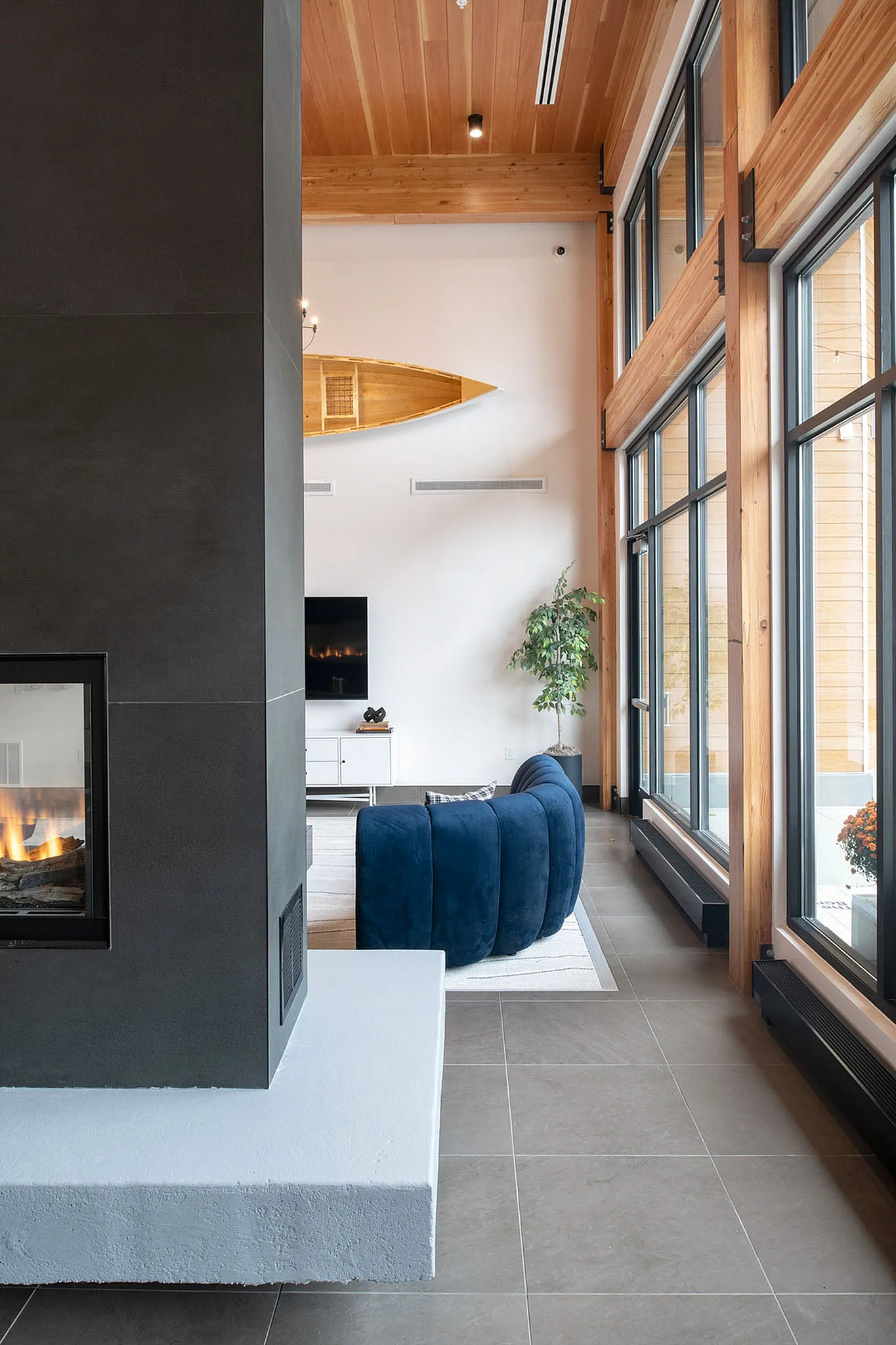 Sophisticated living area with a sleek fireplace, modern blue sofa, and floor-to-ceiling windows offering abundant natural light.