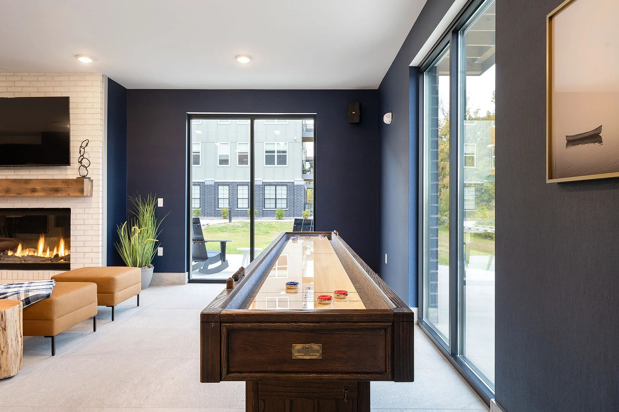 Luxurious lounge with a modern shuffleboard table, elegant fireplace, and large windows offering scenic views.