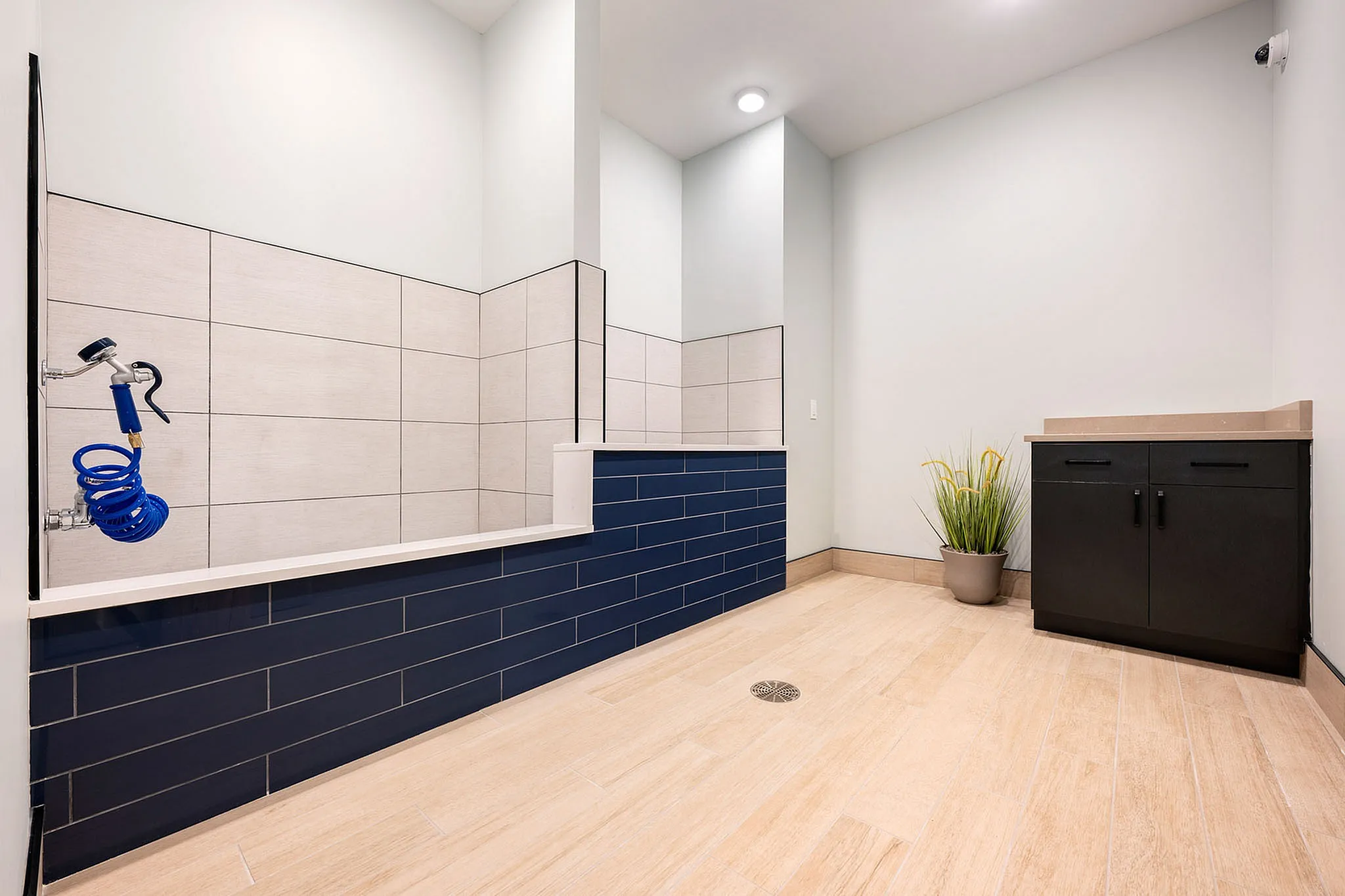 Modern utility room with sleek dark cabinetry, elegant tiled walls, and a convenient spray system, perfect for pet care or cleaning needs.