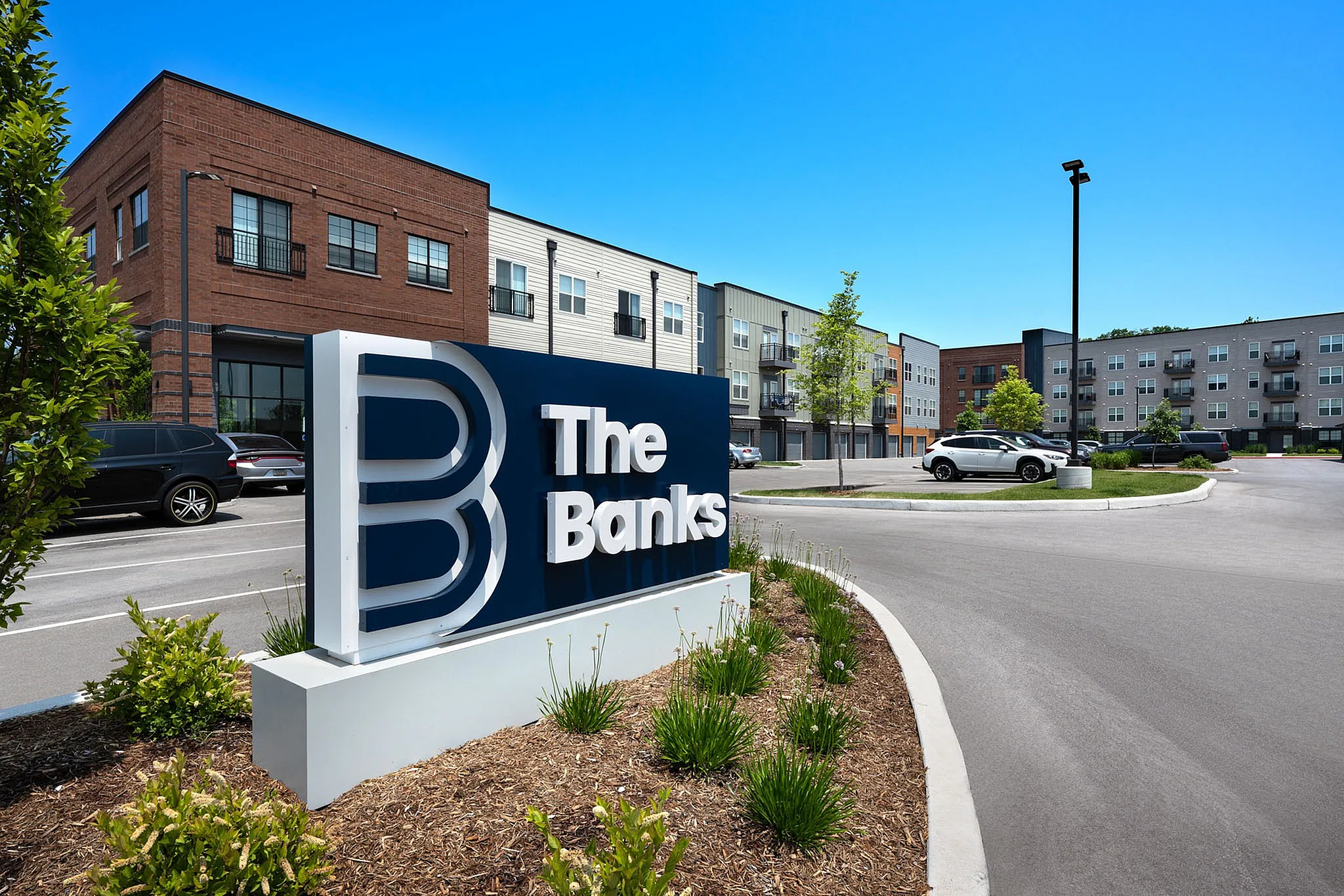 Modern apartment complex with stylish architecture, ample parking, and lush landscaping at The Banks.
