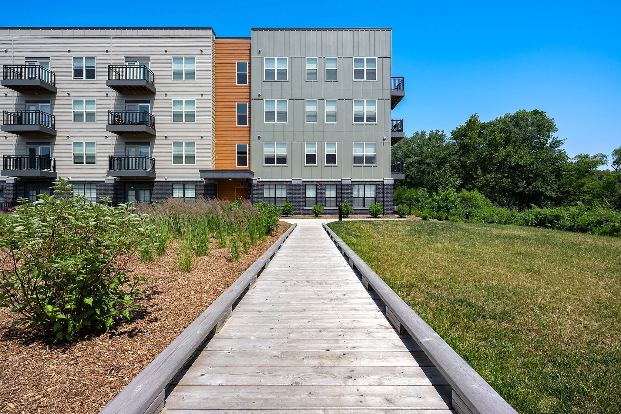 Modern apartment building with stylish exterior, featuring multiple balconies overlooking a lush garden pathway.
