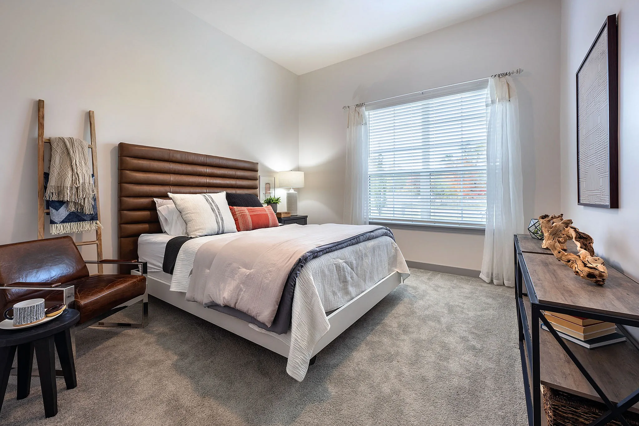 Elegant bedroom with modern leather accents, plush carpeting, and abundant natural light through large windows.
