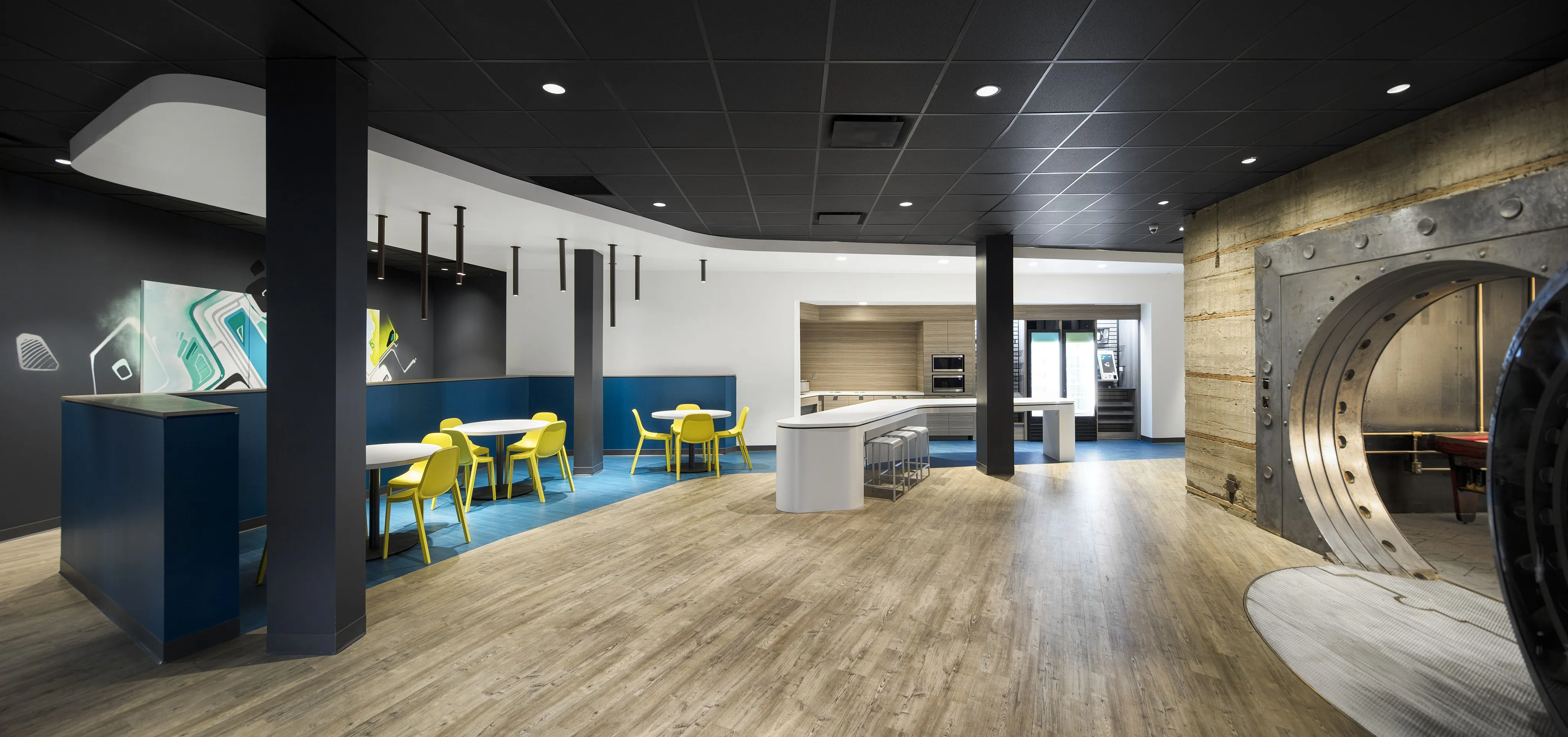 Modern office space featuring sleek design with vibrant yellow chairs, bold blue accents, and an industrial-style vaulted entry.