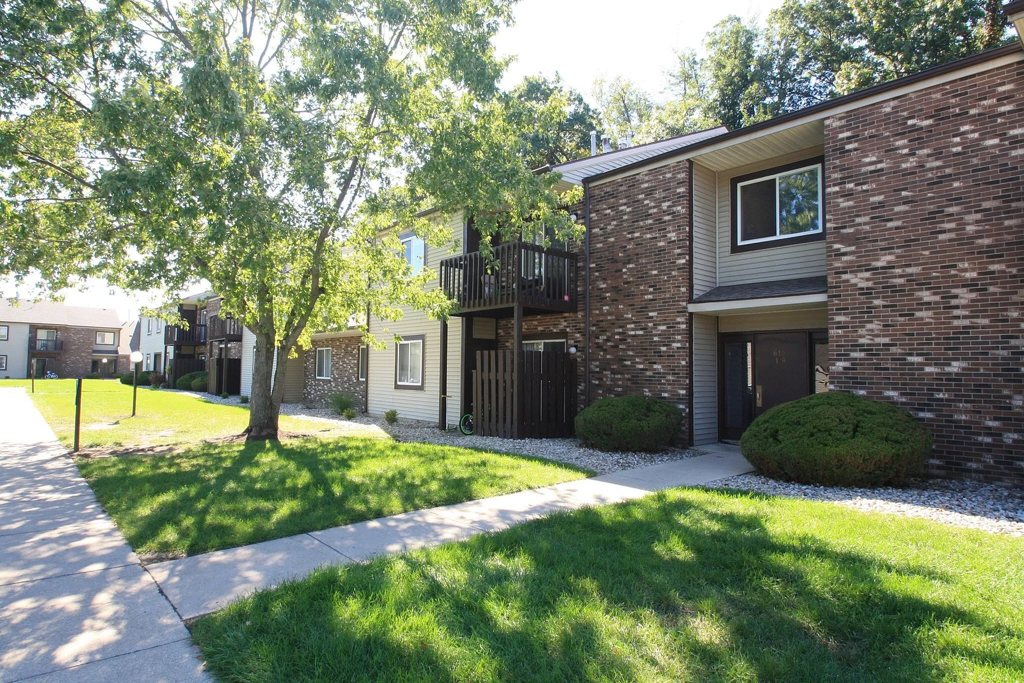 Charming apartment exterior with brick façade, lush green lawn, and mature trees providing a serene setting.