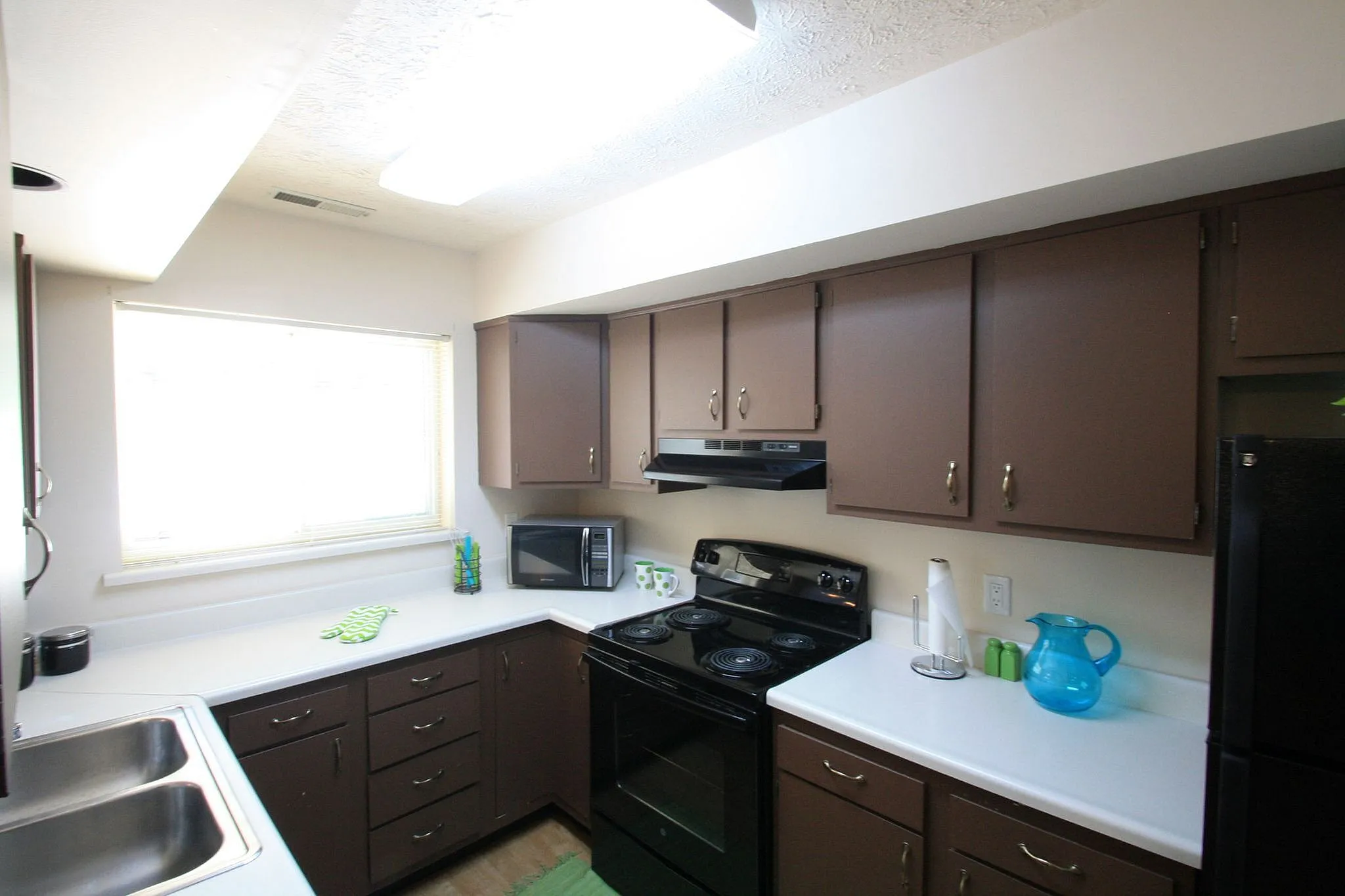Modern kitchen with sleek dark wood cabinets, bright white countertops, and contemporary appliances, offering a stylish and functional cooking space.