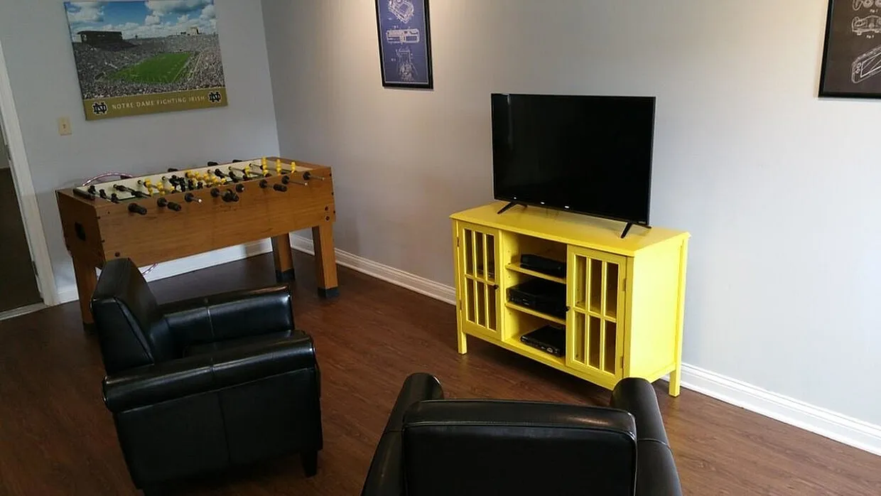 Modern entertainment room with sleek black chairs, vibrant yellow TV stand, foosball table, and stylish wall art.