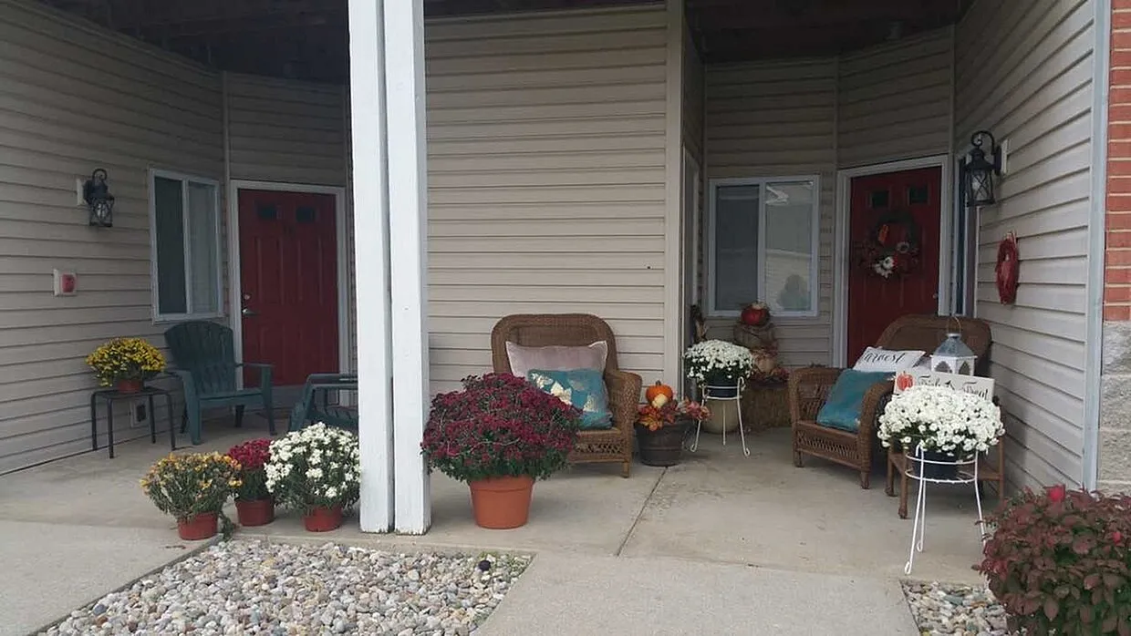 Charming apartment entrance with cozy wicker chairs, vibrant flowers, and inviting red doors creating a welcoming atmosphere.