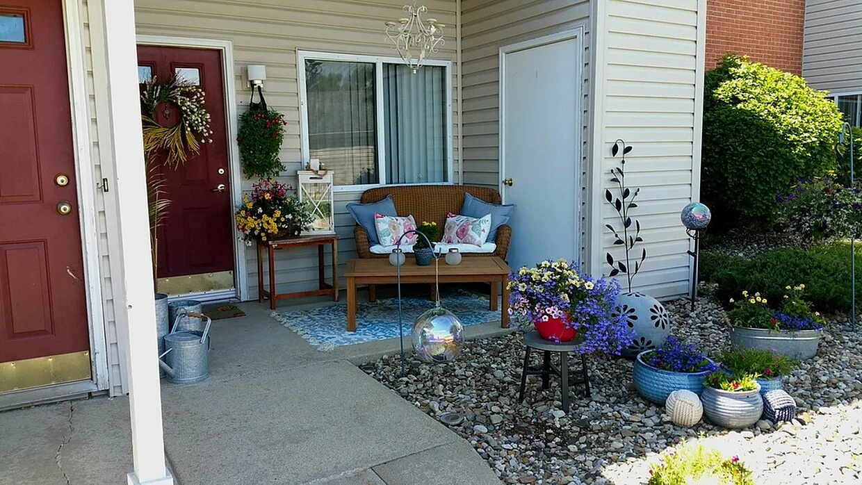 Charming entrance with cozy outdoor seating, vibrant flower arrangements, and a stylish red door, exuding welcoming curb appeal.