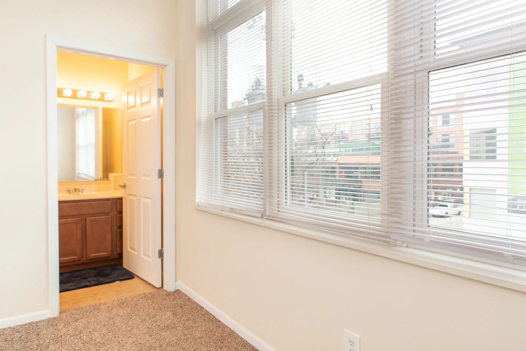 Bright room with large windows featuring city views, plush carpet, and an ensuite bathroom with modern fixtures.