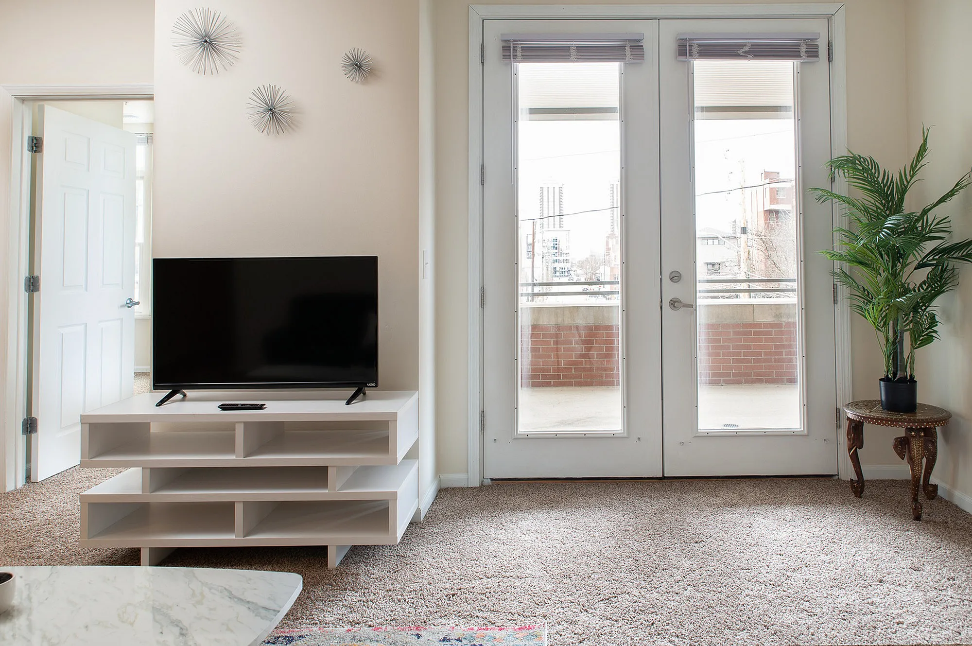 Chic apartment living area with elegant decor, featuring a modern TV stand, decorative wall art, and access to a bright balcony through stylish French doors.
