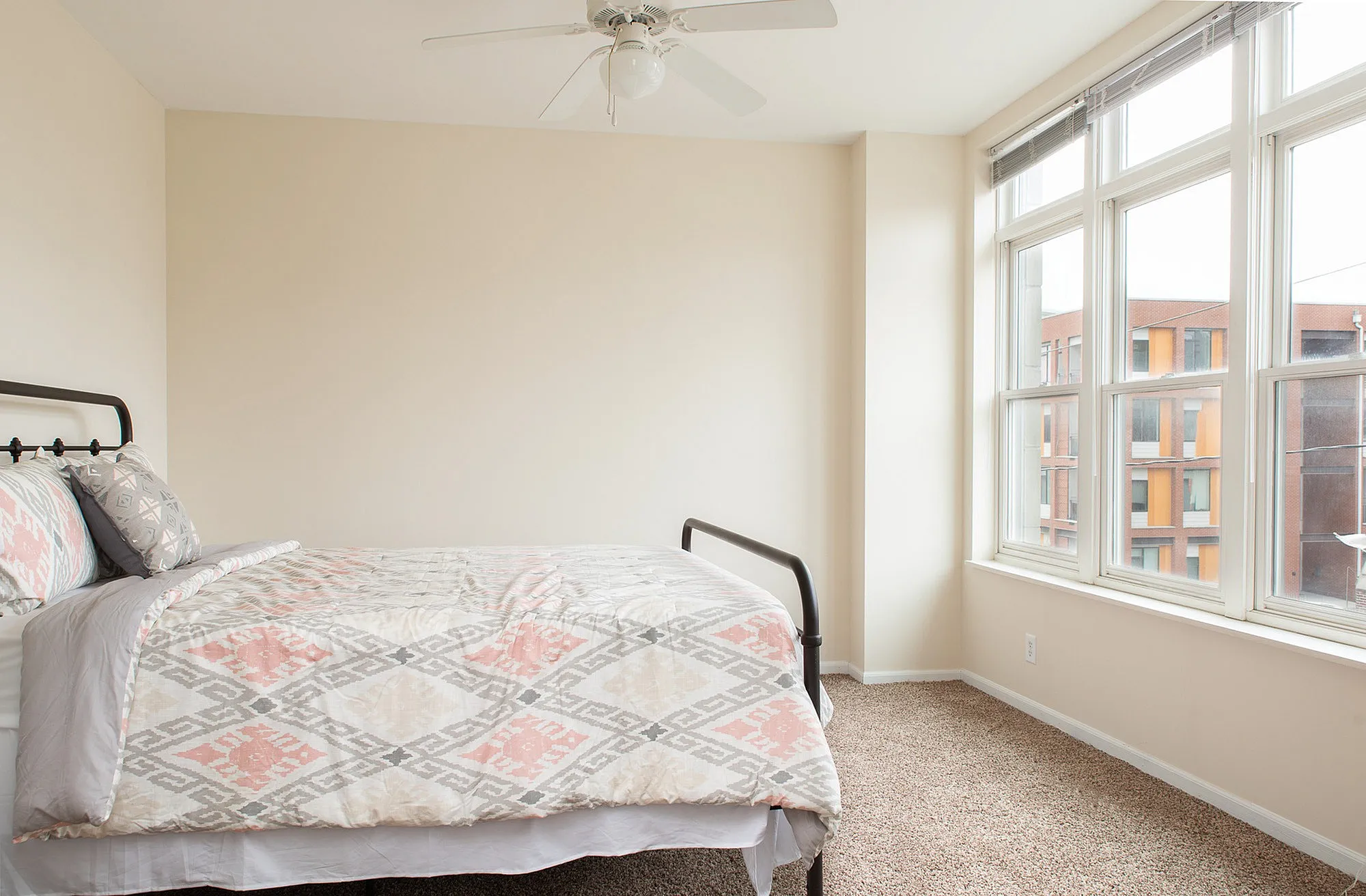 Bright and airy bedroom with a cozy bed, large windows, and modern ceiling fan.