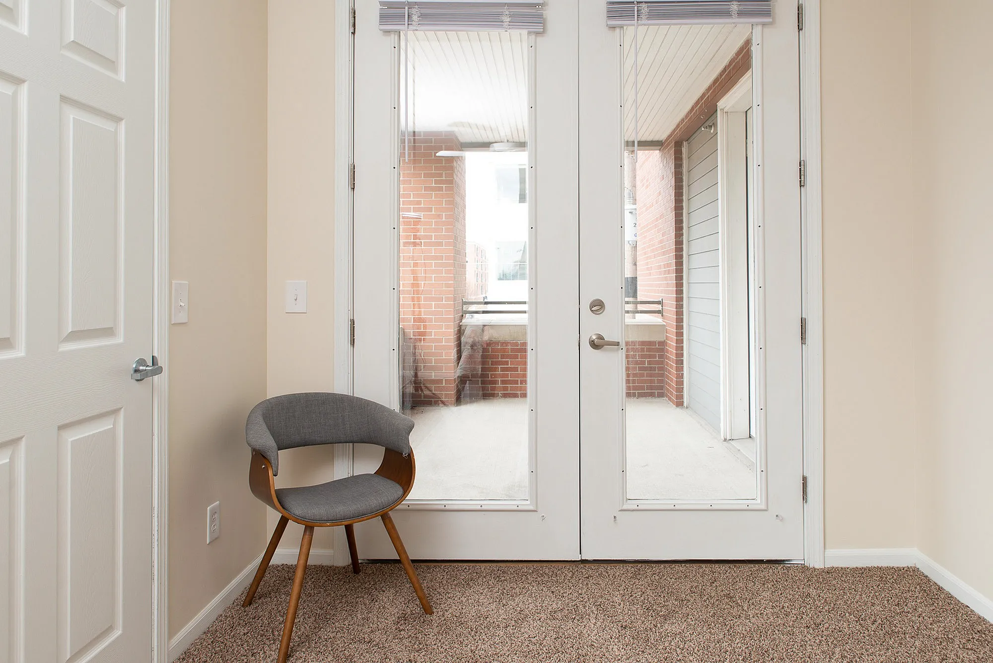 Cozy room featuring stylish chair and glass doors opening to a sunny balcony with brick accents.