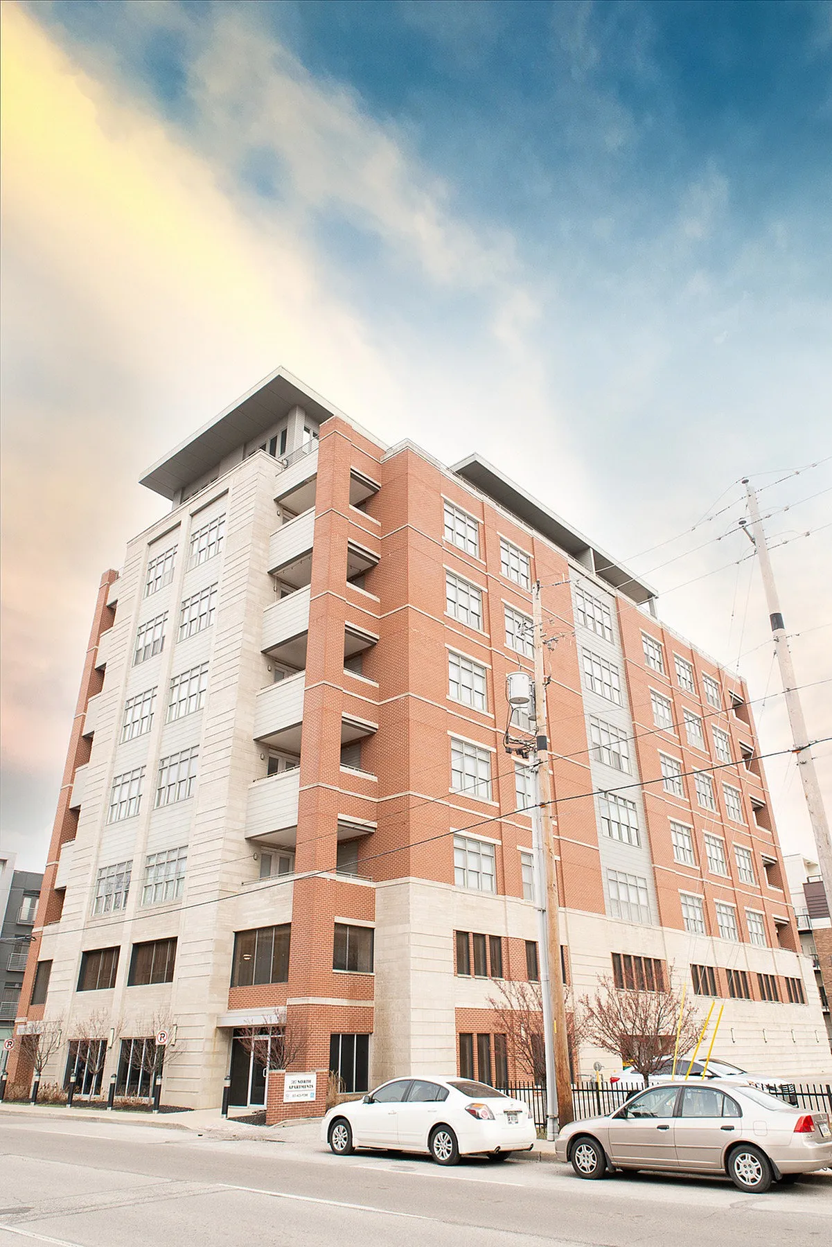 Modern brick and stone apartment building with large windows and balconies against a vibrant sky, ideal for urban living.